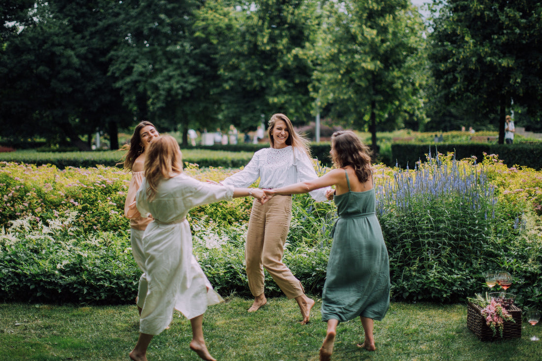Group of women dancing together barefoot outdoors in a garden, celebrating grounding and hormone health